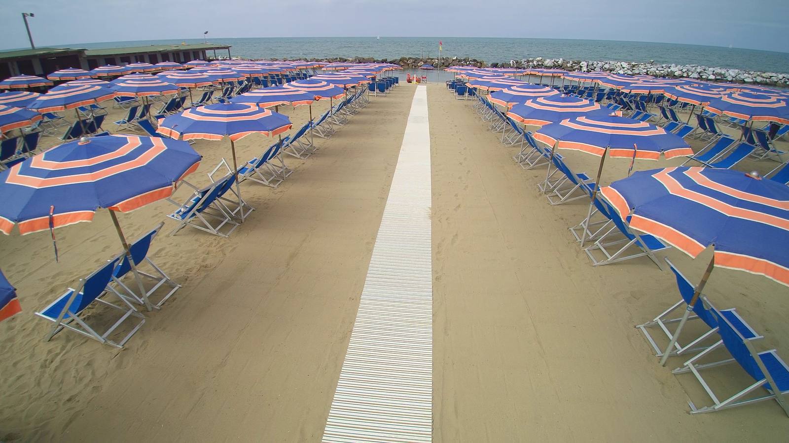 Le file di ombrelloni blu e arancioni del Bagno Azzurro e la passerella che porta al mare, a Marina di Pisa