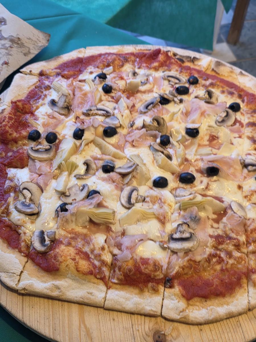 Pizza capricciosa con prosciutto cotto, carciofi, olive e funghi servita sul tagliere alla pizzeria del Bagno Azzurro